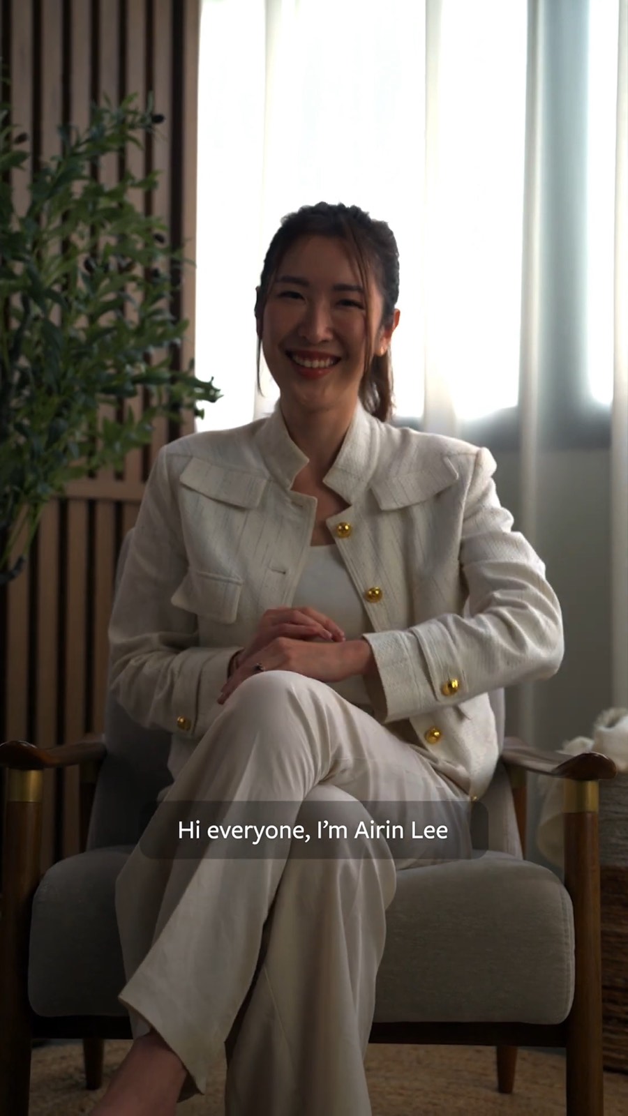 Airin Lee seated in a cream suit, smiling at the camera, in Hello Love’s “Like A Pro” video